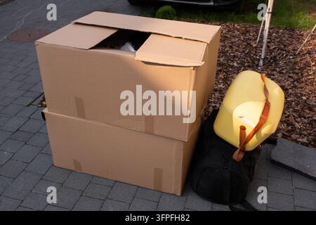 Boîtes de déménagement en carton avec des effets personnels, un réfrigérateur portable jaune et un sac noir posés sur de l'asphalte en plein air Banque D'Images