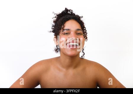 Une femme hispanique montre sa santé cutanée tout en souriant naturellement. Le cadre est simple avec un fond blanc. L'image met l'accent sur l'importance Banque D'Images
