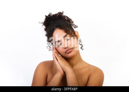 Une femme hispanique montre sa routine de soins de la peau sur un fond blanc. Elle a les cheveux bouclés et affiche une expression douce. Banque D'Images