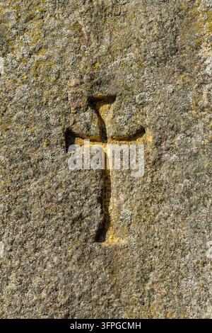Grossissement d'une croix en pierre ancienne sculptée dans une surface rocheuse érodée couverte de lichens jaunes et gris, symbolisant la foi et l'histoire. Banque D'Images