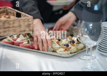 Canapés élégants garnis de jambon sec, d'olives et de pics à cocktail disposés sur un plateau lors d'un événement traité, avec la main d'un invité qui tend à en prendre un Banque D'Images