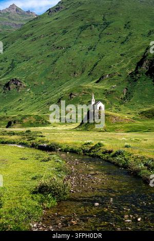 Prise verticale mettant l'accent sur la pittoresque église blanche de Riale, isolée sur sa colline verte luxuriante. Un ruisseau de montagne transparent et caillouteux coule dedans Banque D'Images