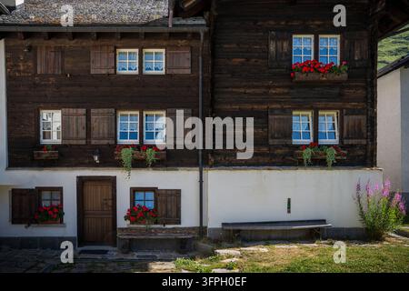 Vue avant de la belle façade d'une cabane alpine traditionnelle à Riale. La structure combine une base enduite de blanc avec des murs en rondins de bois sombre, e Banque D'Images