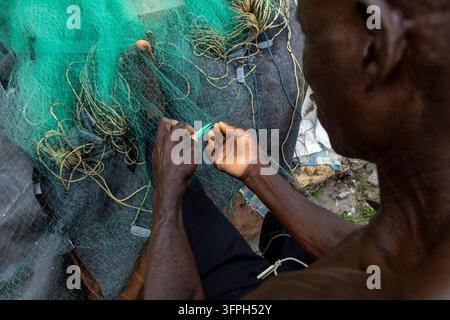 Pêcheur réparant un filet de pêche vert à la main en vue aérienne, Région centrale, Cape Coast, Ghana Banque D'Images