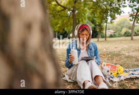 Une femme travaille sur une tablette dans le parc avec son chien. Photo de haute qualitéUne femme travaille sur une tablette dans le parc avec son chien Banque D'Images