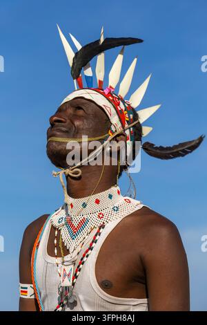 Homme de la tribu Rendille regardant vers le haut portant un bandeau perlé avec des pointes blanches et une plume noire, un collier perlé et un débardeur blanc contre un ciel bleu, M Banque D'Images