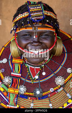 Portrait en gros plan à angle élevé d'une femme souriante de la tribu Pokot portant un voile facial perlé, des boucles d'oreilles en laiton et un grand col décoré de médailles en forme de fleur Banque D'Images
