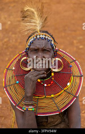 Femme de la tribu Pokot avec un bandeau à plumes et à coquilles de cowrie et un large collier de perles, le menton posé sur la main, comté de Narok, Chepilat, Kenya Banque D'Images