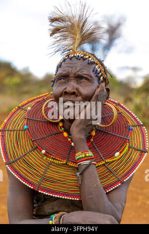Femme de la tribu Pokot avec un bandeau à plumes et coquilles de cowrie et un large collier de perles, regardant vers le haut avec la main sur la joue, Narok, Chepilat, Kenya Banque D'Images