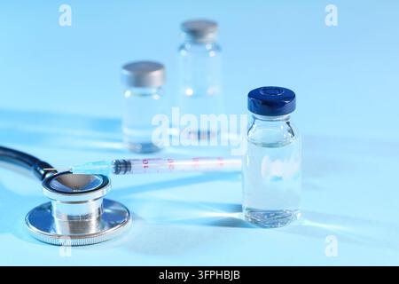 Campagne de vaccination et d'immunisation, flacons médicaux avec seringue et stéthoscope pour la recherche en santé et la prévention des maladies sur fond bleu Banque D'Images