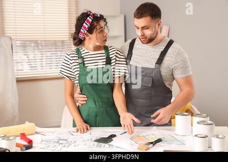 Rénovation intérieure et décoration, jeune couple planifiant l'amélioration de la maison avec des plans et des fournitures de peinture dans un salon lors d'un projet DIY Banque D'Images