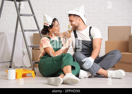 Rénovation de maison et projet de bricolage, jeune couple heureux peignant ensemble les murs dans une nouvelle maison avec des cartons et une échelle pendant l'amélioration intérieure Banque D'Images