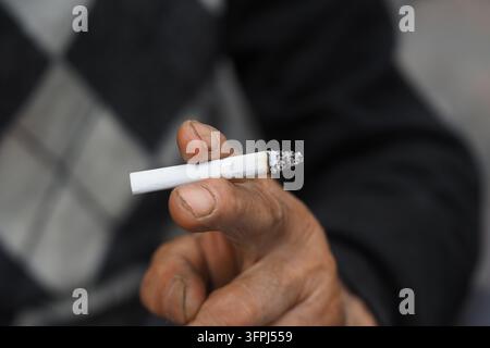 Homme tenant une cigarette à l'extrémité brûlée, main visible, dans un cadre détendu Banque D'Images