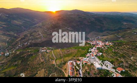 Le coucher de soleil illumine les vignobles en terrasses et un village de colline dans la vallée du Douro au Portugal. Banque D'Images
