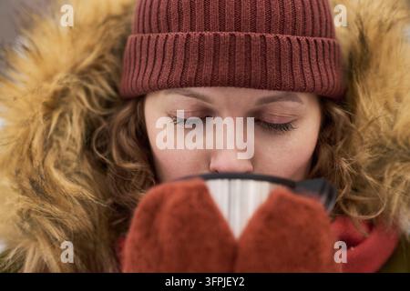 Close-up d'une jeune femme caucasienne buvant du thé chaud en plein air pendant l'hiver. Image adaptée pour un style de vie saisonnier, la publicité pour des boissons et le froid Banque D'Images