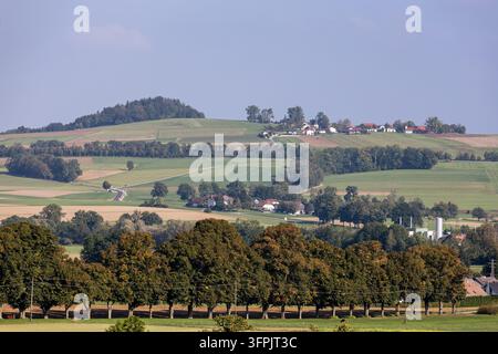 Une vue pittoresque d'un paysage ondulé présentant une ligne d'arbres au premier plan, de vastes champs verts et un charmant village niché dans le d Banque D'Images