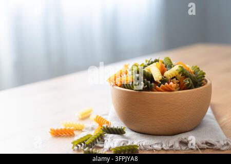 Pâtes fusilli tricolores sèches dans un bol sur une table en bois Banque D'Images