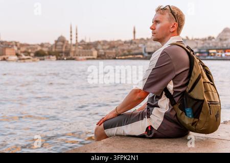 Un jeune homme blond assis sur l'embarcadère et contemplant la skyline d'Istanbul en Turquie. Banque D'Images