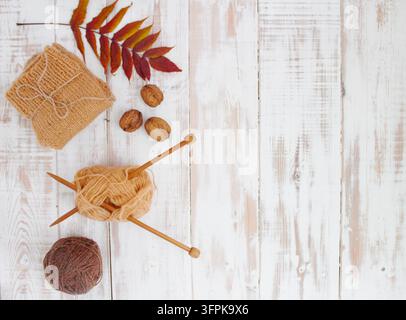 Vue de dessus d'un flat lay tricoté automnal confortable avec des boules de laine, des aiguilles en bois, des chaussettes tricotées, des noix de Grenoble et une feuille d'érable sur un fond en bois blanc avec co Banque D'Images