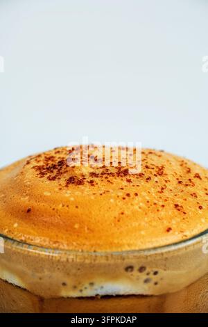 Prise de vue rapprochée détaillée d'un mousseux épais de cappuccino saupoudré de poudre de cacao dans une tasse en verre. Banque D'Images