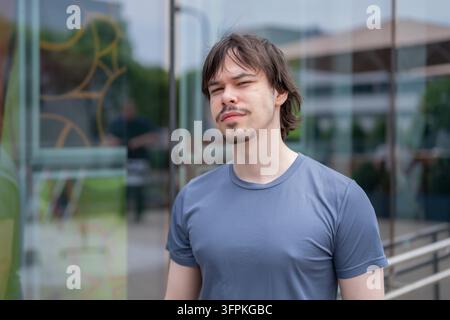Un jeune homme en chemise bleue se tient devant un bâtiment moderne en verre. Banque D'Images