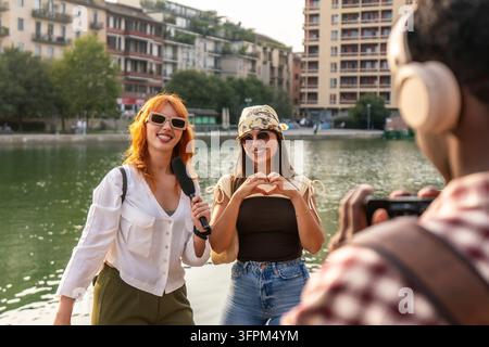 Jeunes amis divers filmant un vlog de voyage à la darsena navigli à Milan, avec une femme parlant dans un microphone et une autre faisant un geste en forme de cœur Banque D'Images