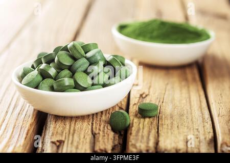 Comprimés de chlorella ou de spiruline dans des tasses blanches sur un fond en bois. Banque D'Images
