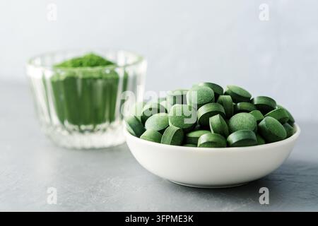 Chlorella ou spiruline sous forme de comprimés et de poudre sur un fond en béton gris. Banque D'Images