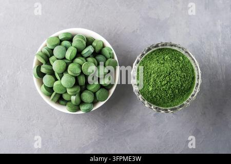 Chlorella ou spiruline sous forme de comprimés et de poudre sur un fond en béton gris. Banque D'Images
