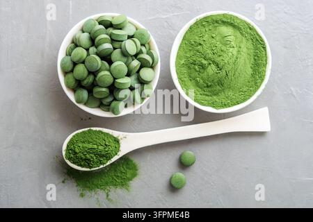 Chlorella ou spiruline sous forme de comprimés et de poudre sur un fond en béton gris. Banque D'Images