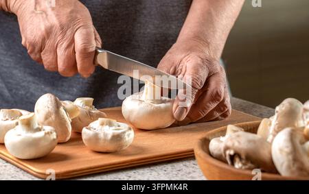 Champignons proches en gros plan. Mains de femme coupant des champignons sur une table en bois. Mains cuisinant des légumes sains. Banque D'Images