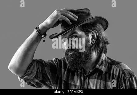 Style cowboy dans une chemise à carreaux. Homme ajustant son chapeau de cowboy. Cowboy non rasé. Cowboy américain. Noir et blanc Banque D'Images