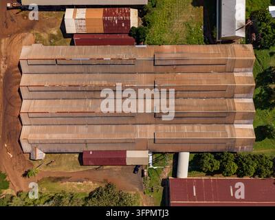 Vue aérienne de la plantation de caoutchouc de Chup avec des bâtiments d'entrepôt industriels dotés de toits en tôle ondulée et des chemins de terre à Tbong Khmum, Tbong Khmum Banque D'Images
