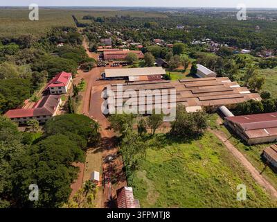 Vue aérienne de la plantation de caoutchouc de Chup présentant des entrepôts industriels avec toits en métal entourés de luxuriante végétation de gommiers et de chemins de terre à Tboung Khmum Banque D'Images