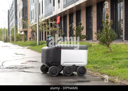 Robot de livraison automatisé moderne debout à l'extérieur attendant une commande par temps pluvieux. Concept moderne de livraison de marchandises au client. Banque D'Images