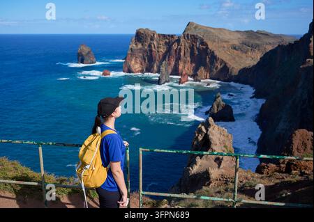Femme avec un sac à dos jaune admire les falaises volcaniques et les îlots rocheux de Ponta de Sao Lourenco, Madère. Concept d'émerveillement, de découverte, de voyage actif et d'appréciation de la nature. Banque D'Images