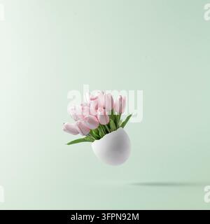 Concept de Pâques. Bouquet de tulipes roses dans un œuf blanc cassé sur un fond pastel bleu. Banque D'Images