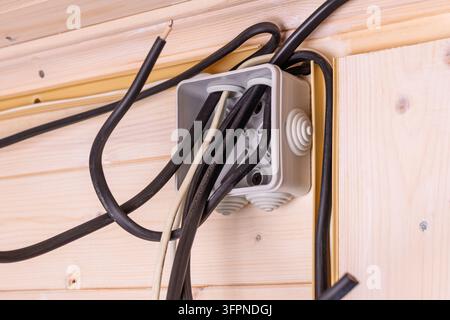 Boîtier électrique ouvert avec plusieurs fils noirs et blancs dépassant d'un mur en bois, montrant l'étape d'installation et l'importance de la sécurité. Banque D'Images