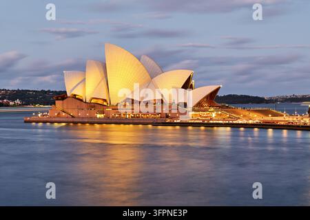 Toits en coquillages illuminés de l'opéra inscrit au patrimoine mondial de l'UNESCO sur Bennelong Point se reflètent dans le port de Sydney pendant l'heure bleue, Nouvelle-Galles du Sud Banque D'Images