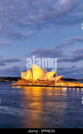 Toits illuminés en forme de voile du centre des arts du spectacle inscrit au patrimoine mondial de l'UNESCO de Jørn Utzon sur Bennelong Point, reflétés dans Port Jackson, Nouvelle-Galles du Sud Banque D'Images