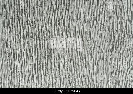 Mur blanc grossièrement plâtré avec des lignes texturées verticales créant un motif abstrait minimaliste sous la lumière naturelle du soleil, évoquant la simplicité urbaine. Banque D'Images