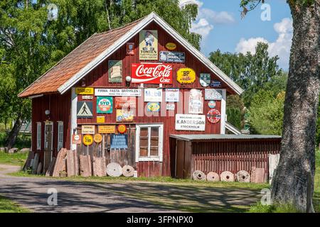 HJO, SUÈDE - 8 JUIN 2013 : Une façade de bâtiment en bois rouge traditionnel recouverte d'une grande collection de panneaux publicitaires vintage en métal. Banque D'Images