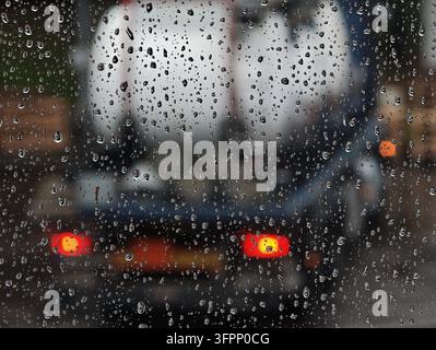 Allemagne. Des gouttes de pluie recouvrent le verre de la fenêtre tandis que le trafic urbain flou brille doucement au-delà, avec des feux de freinage rouges et des reflets de rues mouillées. Banque D'Images
