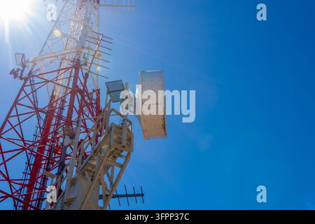 Une tour de communication rouge et blanche avec antennes et paraboles s'élève contre un ciel bleu clair. Banque D'Images