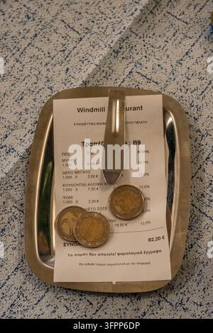 Note de restaurant grecque d'une taverna sur un plateau avec un pourboire en pièces en euros laissé sur la table Banque D'Images