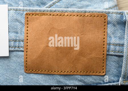 Étiquette en cuir marron vierge sur un jean bleu clair avec étiquette en papier blanc, mockup en gros plan pour la conception de l'identité de marque de vêtements Banque D'Images