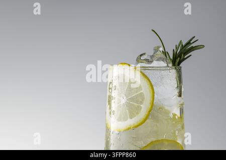 Boisson au citron glacée avec glaçons et romarin dans un verre haut sur fond gris avec espace libre pour un menu d'été ou une publicité pour un bar. Banque D'Images