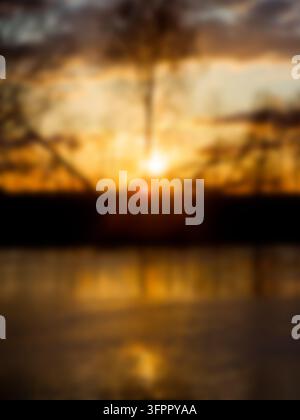 Couchant sur une rivière dorée capturé dans une composition verticale floue, avec des réflexions de lumière douce sur l'eau et des silhouettes d'arbres contre le vibrant Banque D'Images