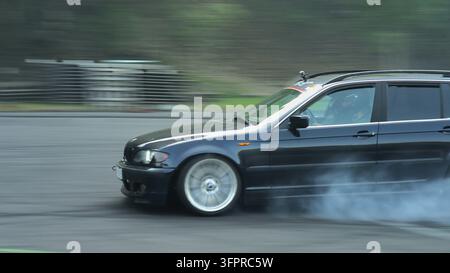 Capture d'action d'une voiture break BMW sombre effectuant un drift, brûlant du caoutchouc et avec des pneus fumants sur une piste asphaltée lors d'un numéro de sport automobile Banque D'Images