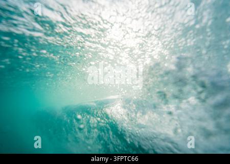 Vue d'une vague se brisant depuis sous l'eau avec la lumière du soleil filtrant à travers l'eau turquoise et des bulles à Newquay, Angleterre, Royaume-Uni. Banque D'Images